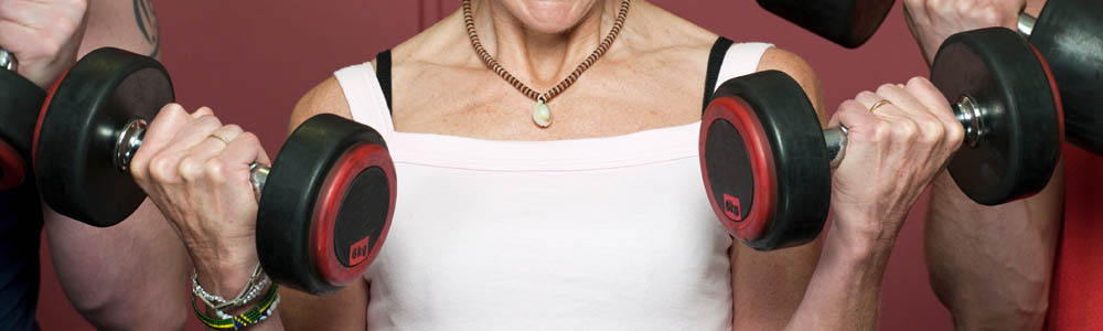 Close-up of torso of woman holding two dumbbells in front of her chest, with two men on either side of her Close-up of torso of woman holding two dumbbells in front of her chest, with two men on either side of her